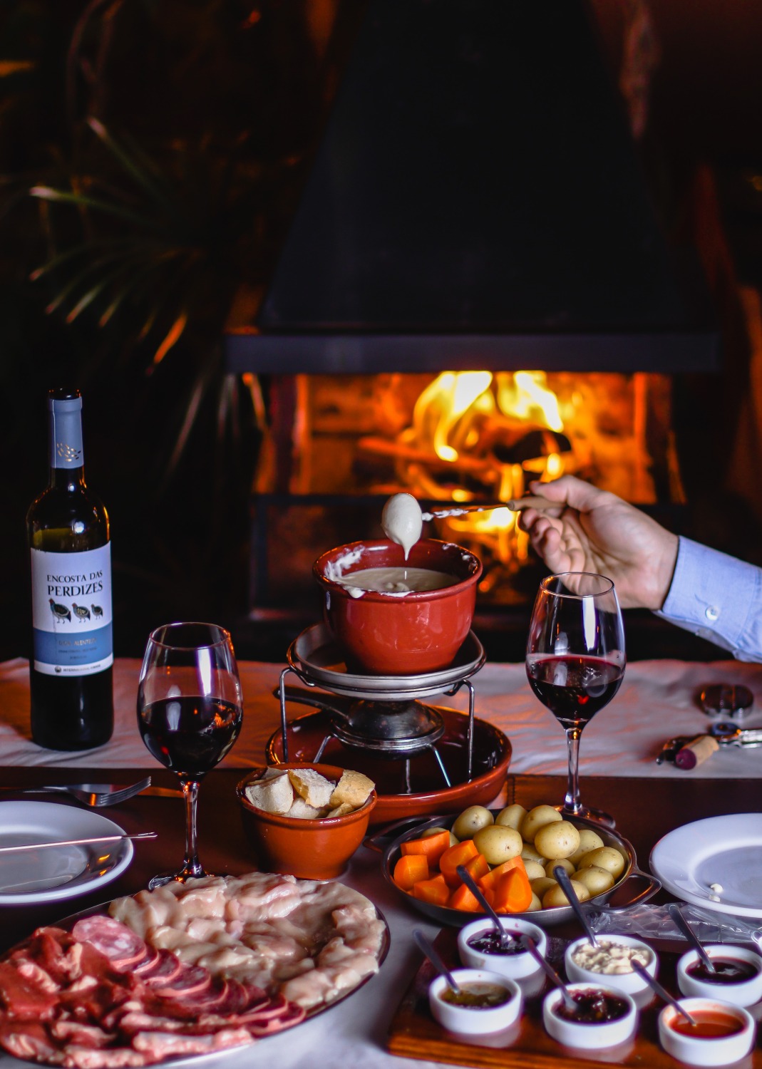 Sequência de fondue de queijo servida à mesa com vinho e lareira